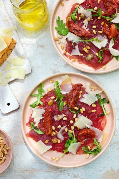 Carpaccio met zongedroogde tomaatjes, rucola en geroosterde pijnboompitjes